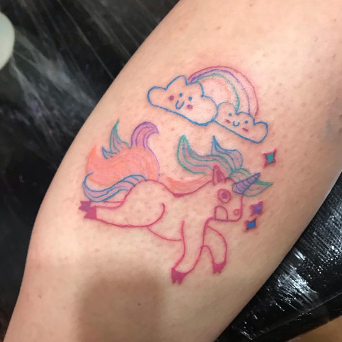 Tatuaje que parece hecho por un niño de un unicornio de colores con nubes y arcoíris hecho por la tatuadora Helen Fernandes