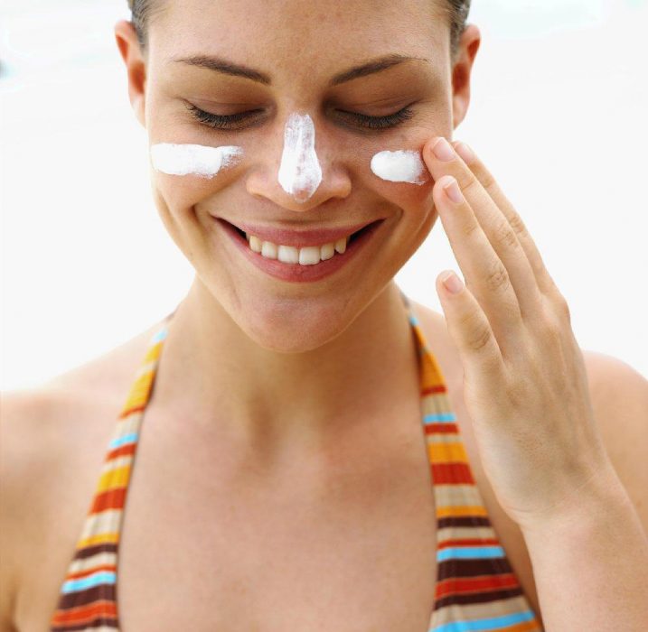 Chica con cabello recogido, traje de baño de colores, aplicando protector solar en su rostro