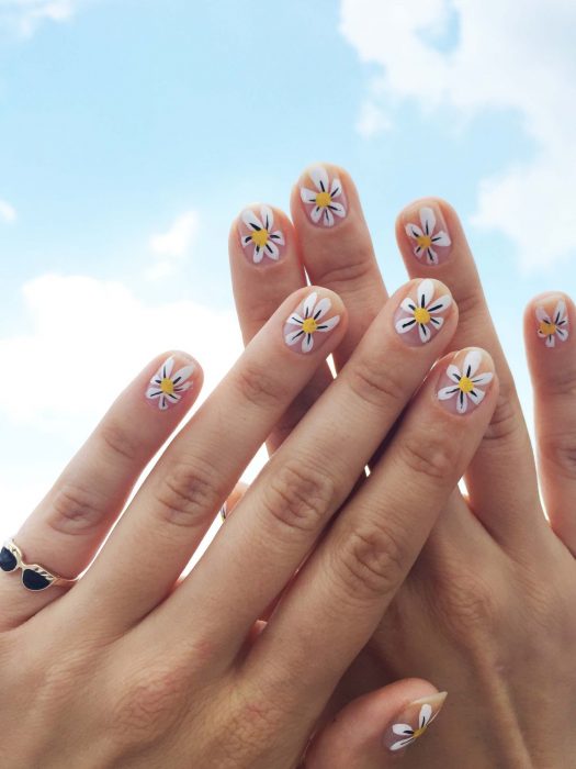 Mano de mujer con uñas con simples flores blancas pintadas que puedes hacer en tu casa para recibir la primavera. anillo de lentes