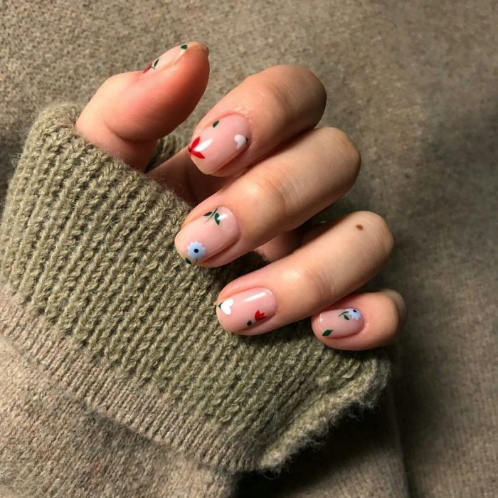 Mano de mujer con uñas pintadas con flores sencillas blancas, azules y rojas con esmalte transparente para la primavera