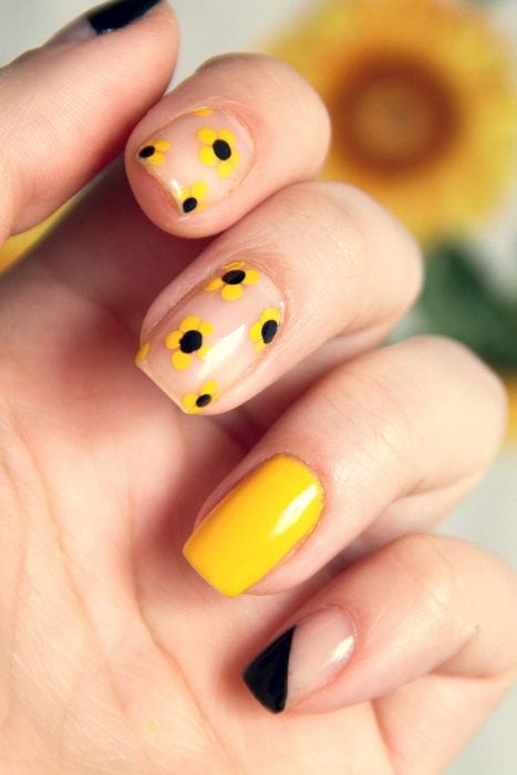 Mano me mujer con uñas pintadas de color amarillo y negro con flores sencillas para primavera