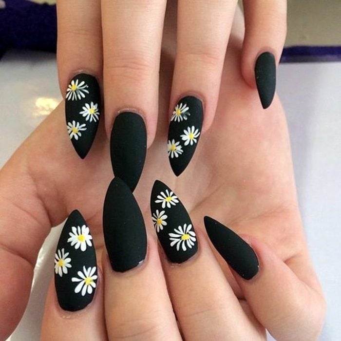 Mano de mujer con uñas largas en forma de almendra pintadas de negro mate con flores margaritas para la primavera