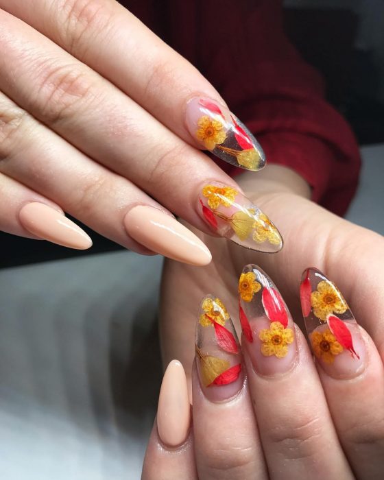 Manos de mujer con uñas largas en forma de almendra pintadas de rosa y transparentes con flores secas reales para la primavera