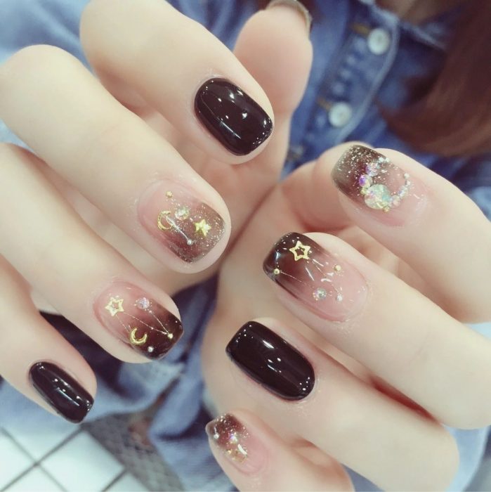 Manicura femenina de constelaciones con esmalte color café sólido y degradado, estrellas doradas y pedrería de fantasía