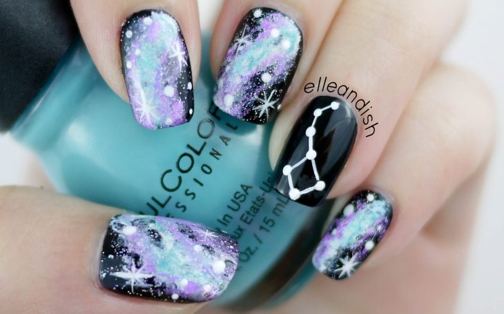 Manicura creativa de constelaciones con esmalte negro, morado y azul creando un universo y estrellas color blanco