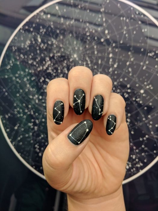 Manicura femenina de constelaciones para uñas largas con esmalte negro con brillos y estrellas blancas