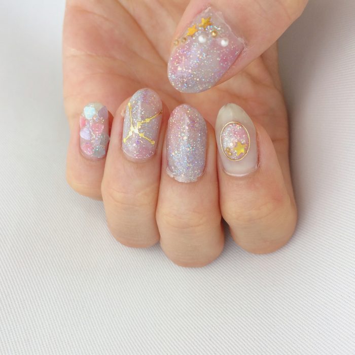 Manicura femenina de constelaciones con esmalte rosa con brillos, estrellas doradas, corazones y cuentas blancas