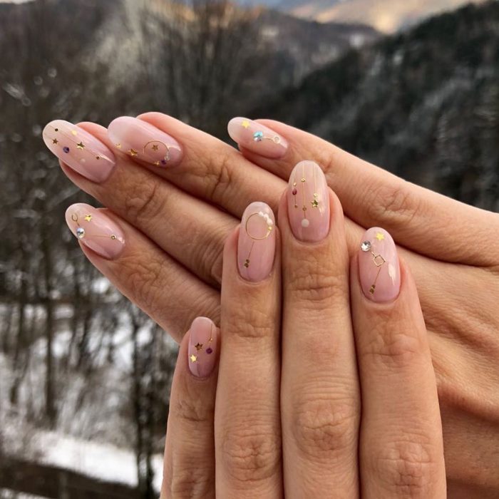 Manicura femenina de constelaciones con esmalte color rosa pálido con estrellas doradas