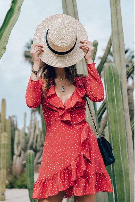 chica cubriendo su rostro con un sombrero con vestido corto rojo con lunares blancos y holanes