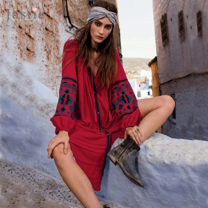 Chica sentada con vestido amplio color rojo, botines cafés y un pañuelo en su frente