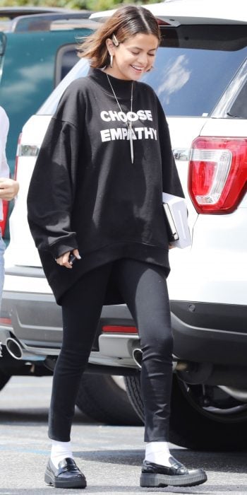 La cantante Selena Gomez caminando por la calle, luciendo unos pantalones negros, sudadera negra holgada y un broche sobre su cabello