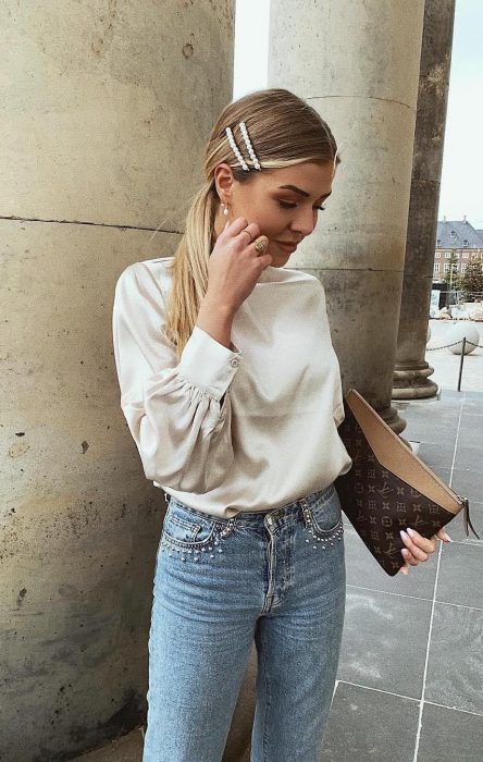 Chica rubia con blusa blanca, jeans de mezclilla y una coleta con dos broches de perlas