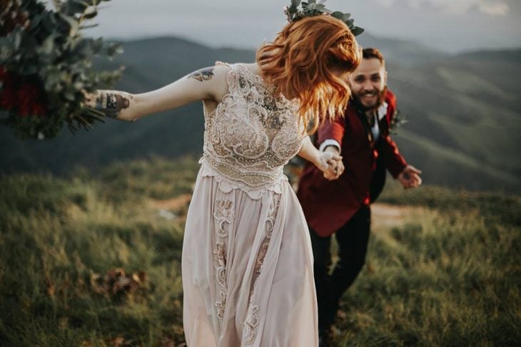 Novios corriendo felices en boda vikinga, chica pelirroja con vestido sin mangas y con perlas