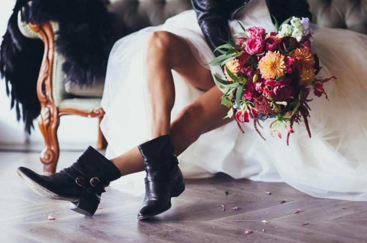 Novia usando vestido blanco esponjoso, sentada en un escalón, mostrando sus botas negras ideales para una boda estilo biker