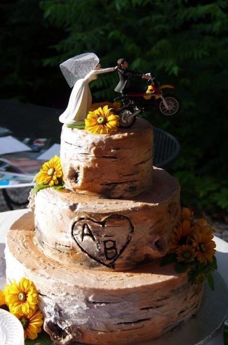 Pastel de boda de tres pisos con poco betún decoradO con girasoles y un par de muñecos en motocicleta, idea para una boda biker 