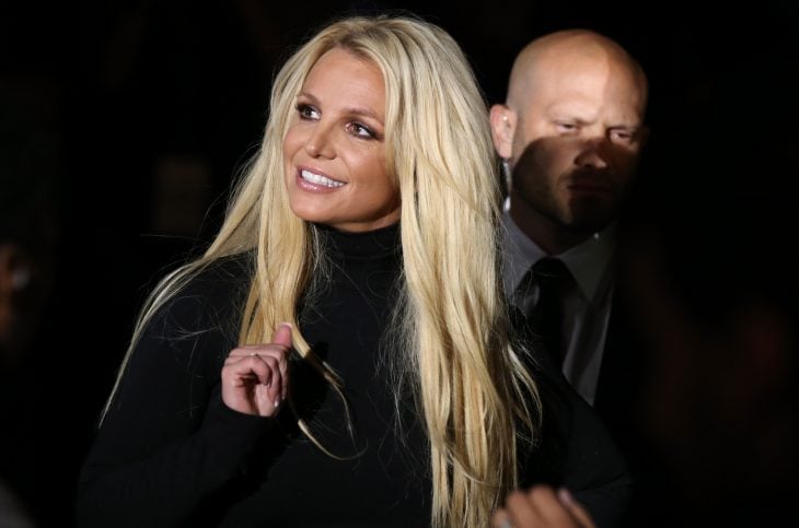 Britney Spears, chica caminando por la alfombra roja, llevando sueter negro, mirando hacia arriba, sonriendo, guiada por sus guardaespaldas