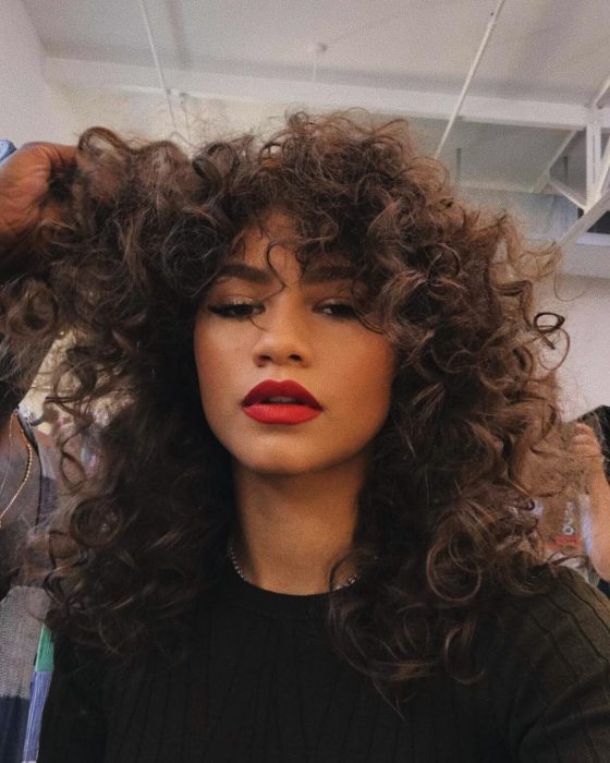 Zendaya, chida de cabello castaño, chino y esponjado usando labial rojo