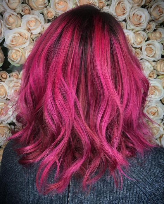 Chica voletada de espaldas, mirando a una pared decorada con flores, mostrando su cabello corto teñido de color bold pink