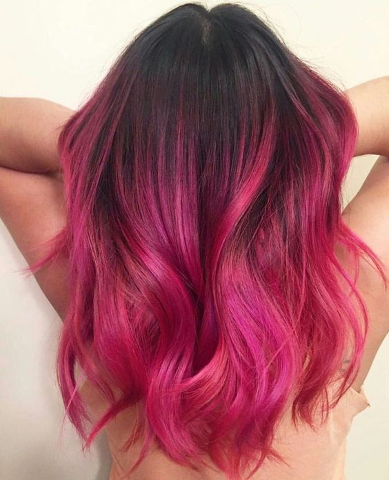 chica volteada de espaldas, acariciando su cabello teñido de color bold pink con ondulados ligeros