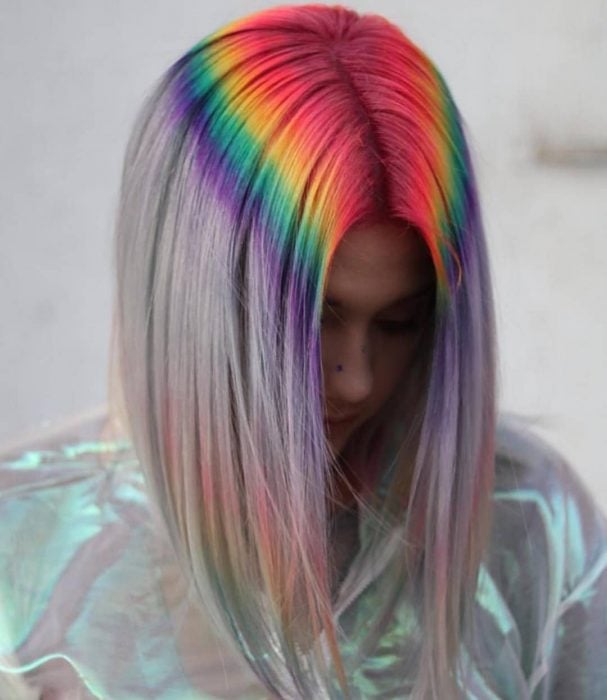 Chica con la cabeza agachada y cabello gris con tintes fantasía en la raíz simulando el reflejo de un arcoíris, rojo, amarillo, verde y morado