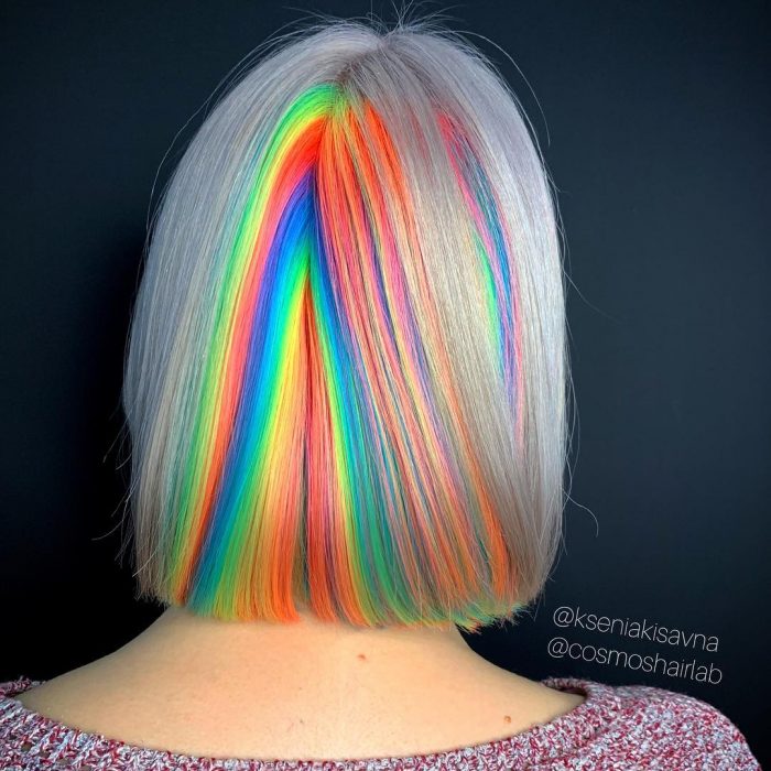 Chica con cabello corto y lacio, teñido de colores fantasía simulando el reflejo de la luz, verde, anaranjado, azul y amarillo