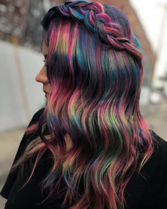 Chica de perfil con cabello ondulado peinado con una trenza y colores de fantasía oscuros, rosa, verde, azul y morado 