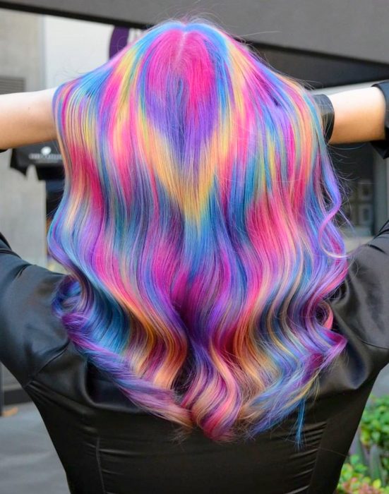 Chica con cabello largo pintado con colores de fantasía que parecen destellos de luz, rosa, azul, morado y amarillo