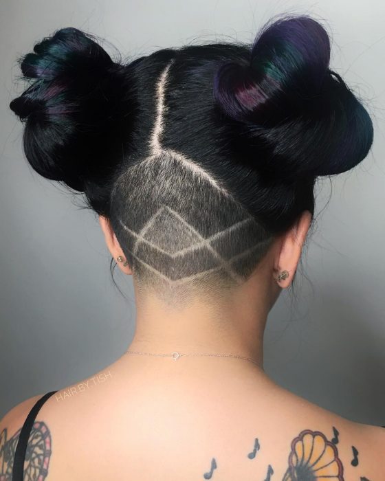 Tendencia de cabello, tinte oil slick que parece aceite derramado en el suelo, chica con cabeza rapada de atrás con figuras geométricas, con dos chongos altos, cabello color negro con reflejos morados y verdes