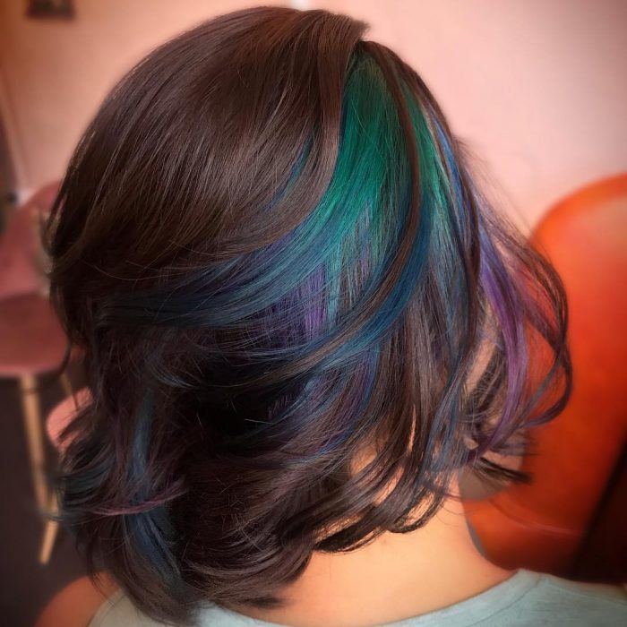 Tendencia de cabello, tinte oil slick que parece aceite derramado en el suelo, chica con la mitad del cabello pintado de colores morado, azul y verde