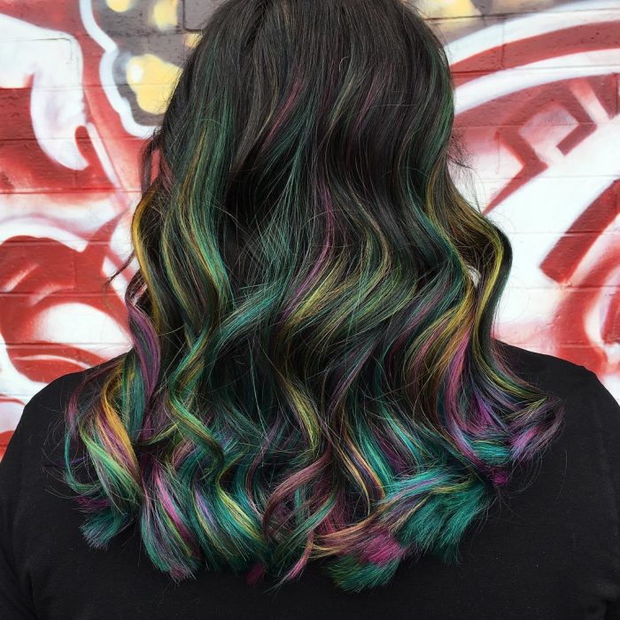 Tendencia de cabello, tinte oil slick que parece aceite derramado en el suelo, chica de cabello largo y ondulado de colores amarillo, verde, rosa, morado y azul