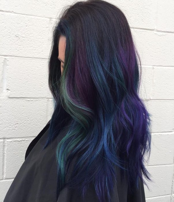 Tendencia de cabello, tinte oil slick que parece aceite derramado en el suelo, chica de cabello oscuro y largo con tonalidades verde, morado y azul