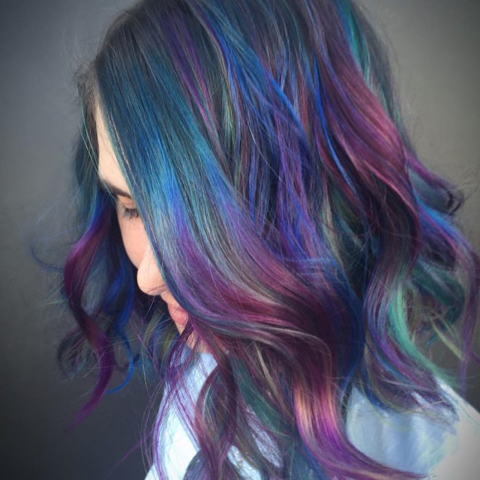 Tendencia de cabello, tinte oil slick que parece aceite derramado en el suelo, chica con cabello corto, ondulado y de color azul morado, verde, rosa y amarillo