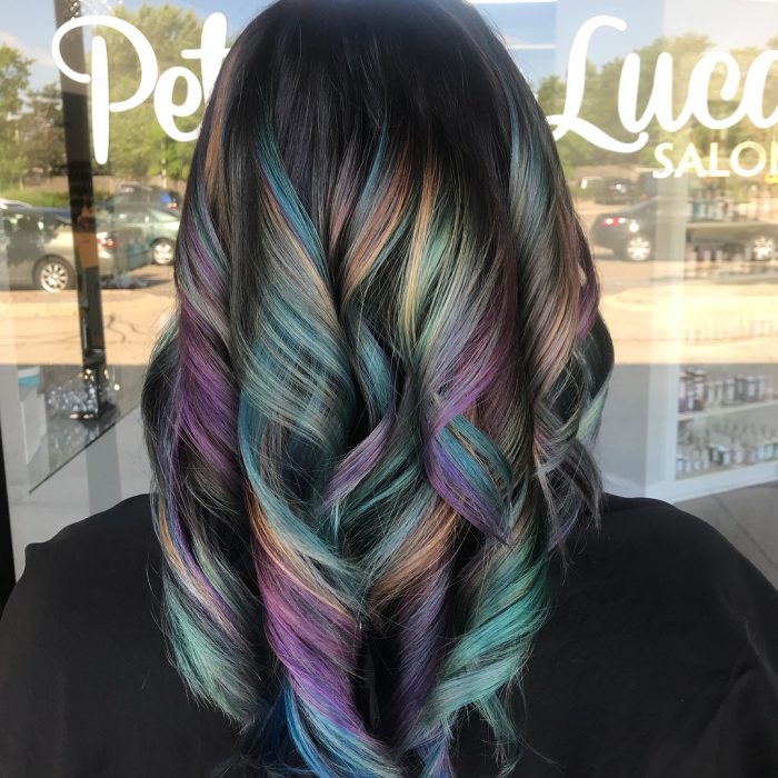 Tendencia de cabello, tinte oil slick que parece aceite derramado en el suelo, mujer con cabello de indas grandes, de color morado, verde, azul y anaranjado