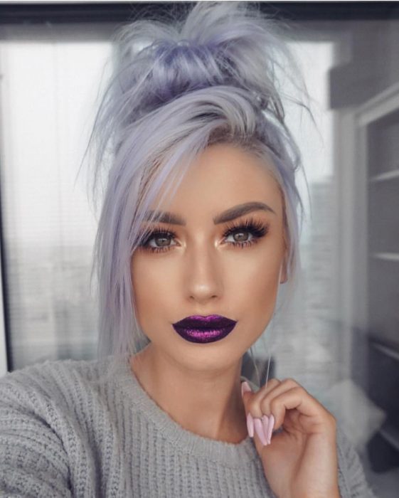 Mujer con pestañas postizas y labial color morado metálido, con cabello color gris lavanda o lavender gray con un chongo alto despeinado