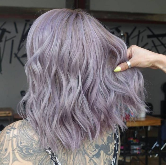 Chica con tatuajes en la espalda y cabello corto a los hombros y ondulado, color gris lavanda o lavender gray