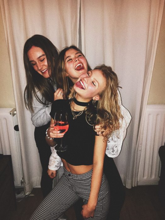 Tres amigas riendo mientras se abrazan y beben una copa de vino rosa
