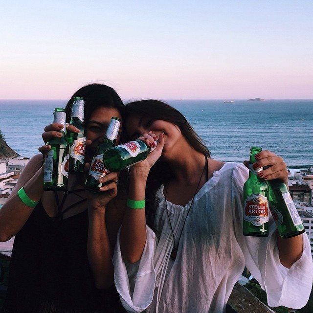 Amigas en la orilla de la playa bebiendo cerveza con ambas manos 
