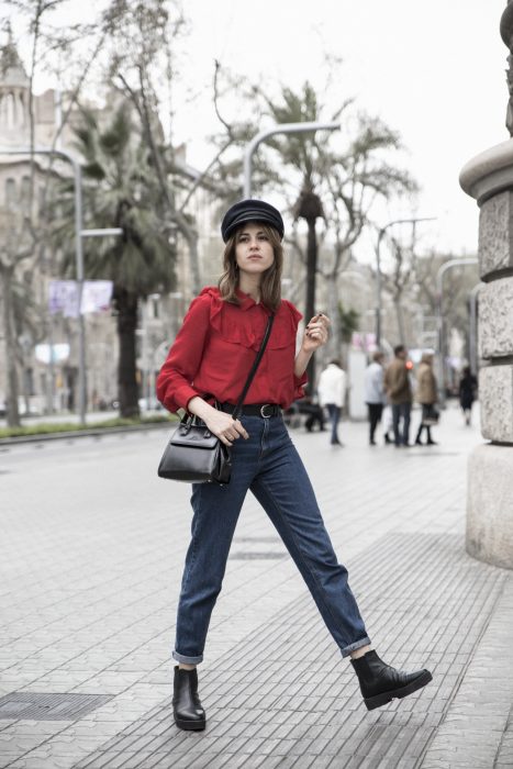 Chica modelando una blusa holgada roja, pantalón de mezclilla, bolso negro y sombrero negro