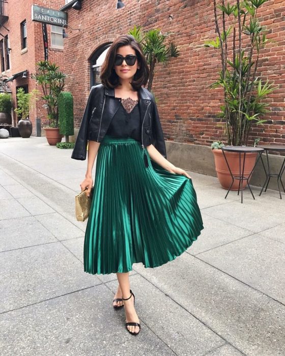 Chica caminando por la calle con un atuendo de falda verde holgada, una camiseta negra, gafas negras y sandalias de tacón