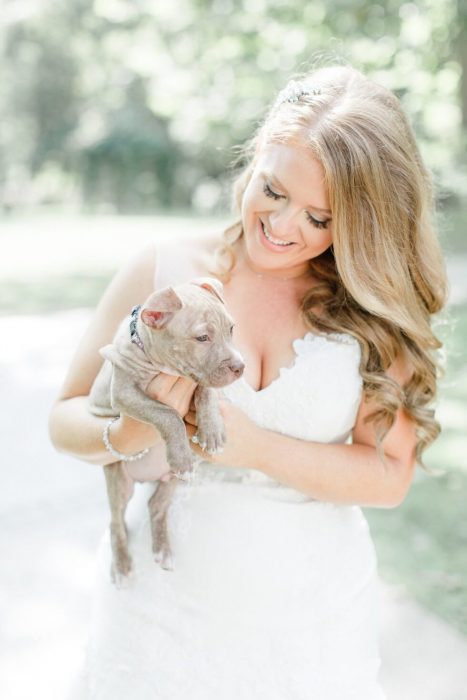 Novia sosteniendo un cachorro pit bull entre sus manos en vez de su ramo de flores 