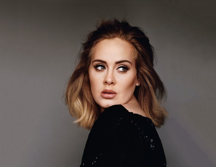 Adele con fondo gris, de perfil, vestido negro, posando para una fotografía, con cabello midi balayage