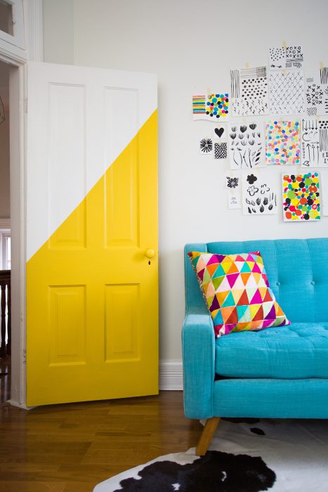 Door of a room that is on the side of a blue sofa decorated in half with yellow paint