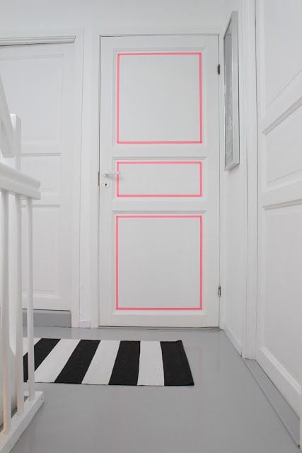 Puerta blanca decorada con líneas de color rosa en los cuadros que la forman 