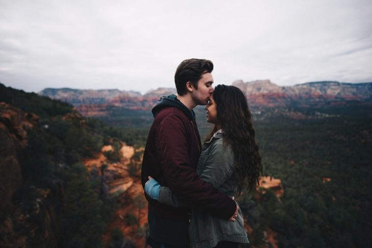 Pareja de novios en la cima de una montaña, abrazados, besando sus frentes como gesto de amor 