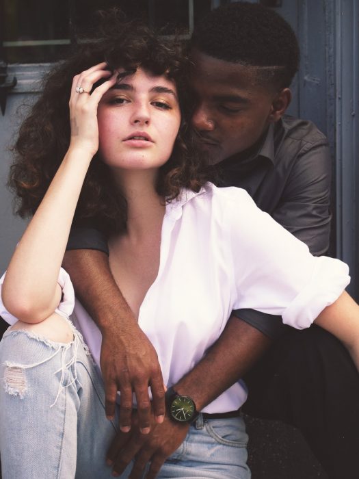 Pareja interracial abrazados, sentados en un portico de madera, posando para una fotografía