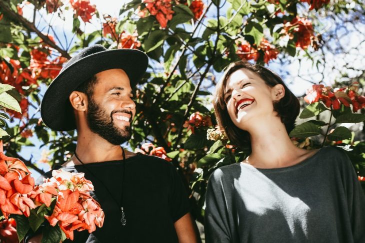 Pareja de novios bajo las ramas de un cerezo en flor, sonriendo y posando para una foto