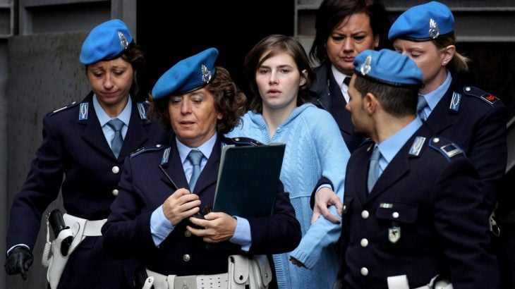 mujer con cabello corto, portando pants deportivo colro azul cielo, siendo custodiada por un grupo de policías vestidos de azul marino, Escena del documental Amanda Knox 