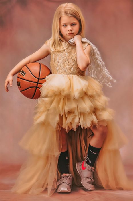 Niña sosteniendo una pelota de basquetball usando vestido de olanes estilo princesa fotografía por Heather Mitchell