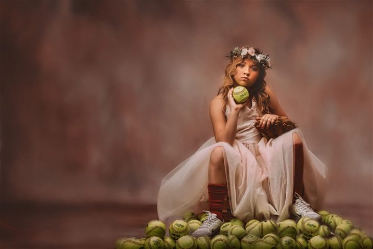 Niña sosteniendo pelotas de tenis sentada en el suelo usando corona de flores y vestido estilo princesa 