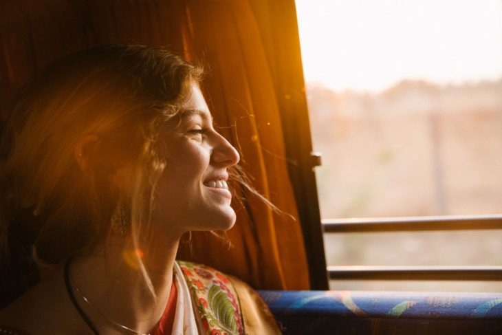 Chica sonriendo felizmente mientras ve el paisaje soleado a través de una ventanilla